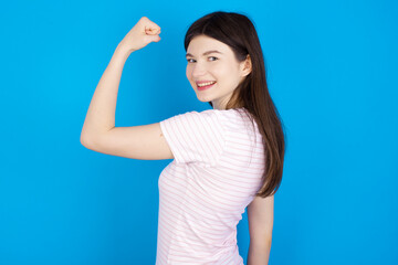 Portrait of powerful cheerful young beautiful Caucasian woman wearing stripped T-shirt over blue...