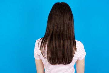 The back view of a young beautiful Caucasian woman wearing stripped T-shirt over blue wall. Studio Shoot.
