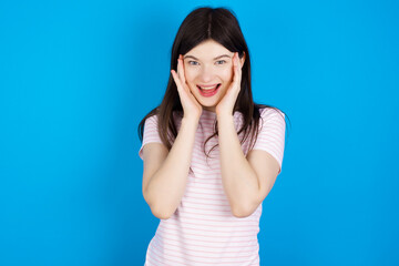 young beautiful Caucasian woman wearing stripped T-shirt over blue wall Pleasant looking cheerful, Happy reaction