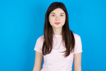 Obraz premium Stunned young beautiful Caucasian woman wearing stripped T-shirt over blue wall stares reacts on shocking news. Astonished girl holds breath