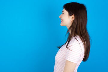 Profile portrait of nice young beautiful Caucasian woman wearing stripped T-shirt over blue wall...