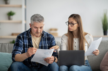 Frustrated mature couple with laptop computer checking financial documents at home