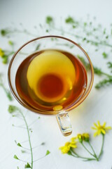 Green tea in a glass cup on white. Herbs and flowers around a mug with a healthy drink