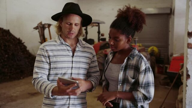 Mixed race male and female farmers standing in bard shed discussing plans using digital table 
