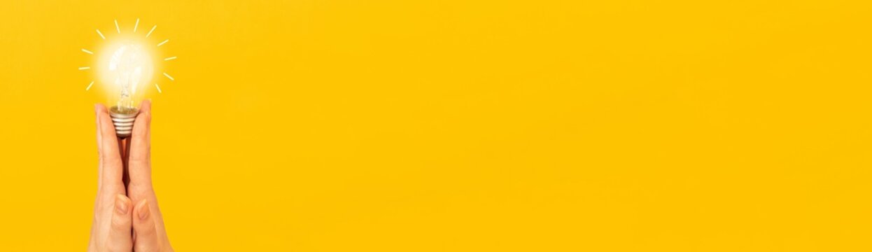 New idea concept and mockup banner with orange background, lit light bulb in woman hand, copy space, innovation and creativity
