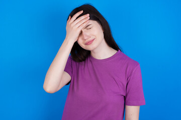 A very upset and lonely young beautiful Caucasian woman wearing purple T-shirt over blue wall crying,