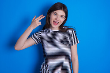 Fototapeta premium young beautiful Caucasian woman wearing pink jacket over blue wall foolishes around shoots in temple with fingers makes suicide gesture. Funny model makes finger gun pistol