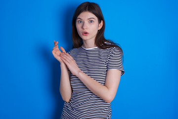 Fototapeta premium Surprised emotional young beautiful Caucasian woman wearing pink jacket over blue wall rubs palms and stares at camera with disbelief