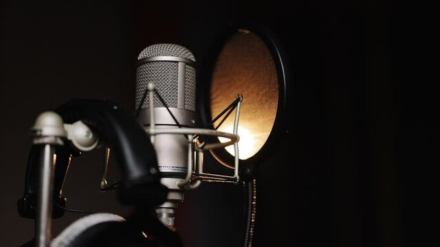 Studio recording, professional microphone in the recording studio, microphone near wall with acoustic dampening foam. Close-up of microphone on stage against a black background with lighting