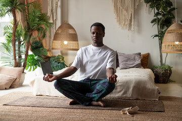 Young african man meditating sitting at his bedroom in the morning