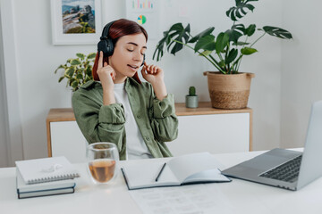 Woman listening music with wireless headphones. Young businesswoman relaxing at comfortable workplace. Concept of resting during online business at home office,telework or studing. Happy girl singing