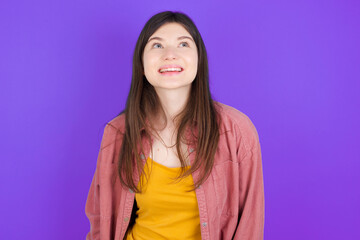 Surprised young beautiful Caucasian woman wearing casual clothes over purple wall, shrugs shoulders, looking sideways, being happy and excited. Sudden reactions concept.