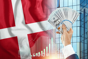 Money in a man's hand against the background of the flag of Denmark. Danish income. Financial...