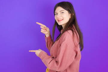 young beautiful Caucasian woman wearing casual clothes over purple wall points aside with  surprised expression with mouth opened, shows something amazing. Advertisement concept.