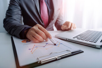 Cropped shot group of businesspeople using graph chart and computer laptop, tablet discussing about business plan together in modern office.