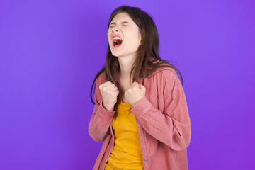 young beautiful Caucasian woman wearing casual clothes over purple wall excited and glad to achieve victory, clenches fists, screams in excitement with closed eyes,successful person.