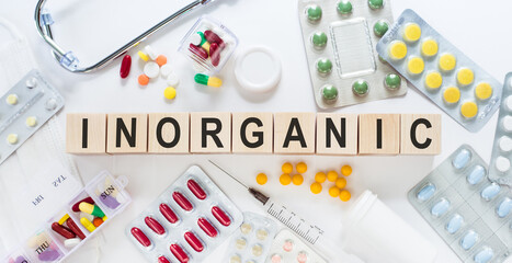 INORGANIC medicine word on wooden blocks on a desk. Medical concept with pills, vitamins, stethoscope and syringe on the background.