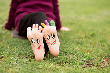 Child have fun outdoor on grass. Feet of child with painted smile faces.