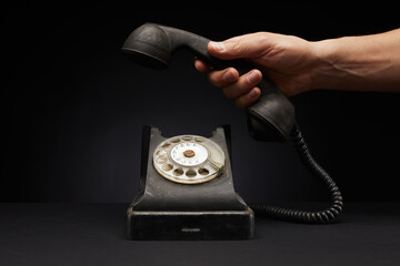 Male hand holding vintage black telephone receiver isolated on black background - obrazy, fototapety, plakaty