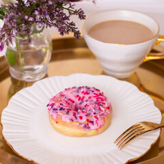 Coffee cup and sweet strawberry donut on golden plate with flower bouquet