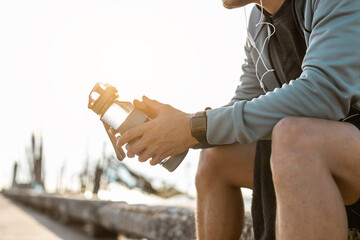 Tired man is sitting and holding water bottle after run in the morning.