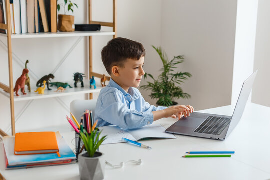 Clever kid doing homework using laptop and internet. Elementary school e-learning via video call. Boy studying online at home