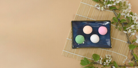 Japanese traditional confectionery. Set of matcha mochi with blossom on bamboo mat on beige table. Healthy rice sweets. Ice cream.  Spring flatlay for restaurant menu, receipt.  Top view, copyspace