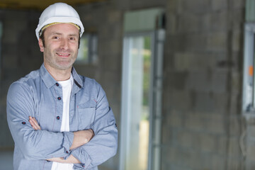 happy young man builder in helmet standing with arms crossed