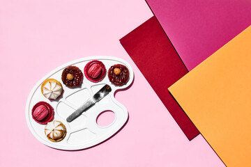 Creative still life of colorful macarons as a form of colors on art palette. Minimal abstract concept. Macarons pastry almond sweet on pink background