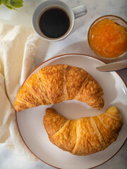 family breakfast, croissants close-up, white porcelain plate, porcelain bowl, orange jam, porcelain white cup, coffee. Delicious and healthy breakfast