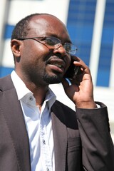 Young businessman of African origin standing outdoors, on his cellphone speaking