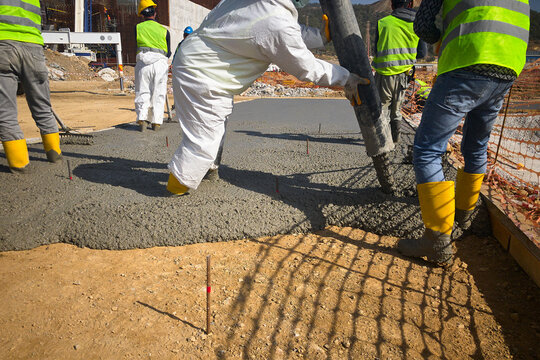 Construction workers dressed in uniform pour a concrete to formwork. Cement works on a construction site