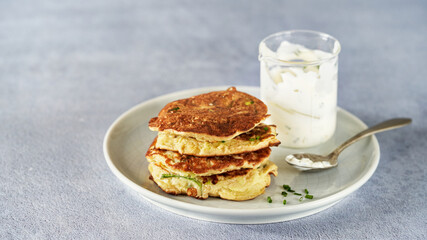 Vegetable zucchini fritters in stack with sour cream and chive, light background, copy space. Healthy clean vegetarian food.