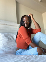 mid angle view of young black woman looking straight at camera, close up portrait, african american woman, long hair,background, beautiful complexion,one person, dark orange color, jeans and t-shirt