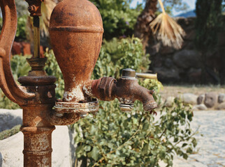 Old and rusty vintage water pump with stainless bucket.  traditional watering fountain in garden.