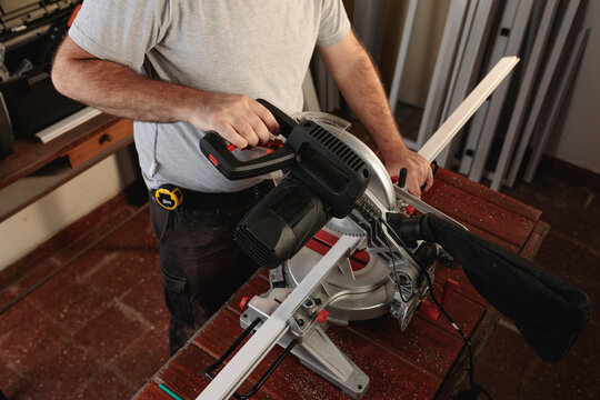 Top view of part of the body of a male carpenter, using a miter saw to cut aluminum profiles.