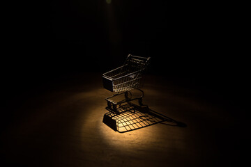 Empty shopping trolley on dark toned foggy background with some copy space. Financial crisis...