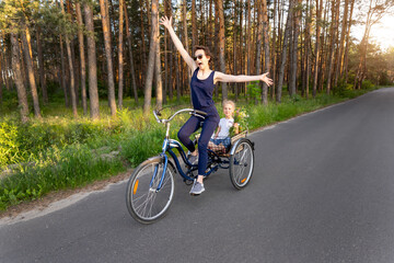 Young adult caucasian mom enjoy having leisure fun riding bicycle with cute adorable blond daughter holding wild field flower at scenic rural country road on bright sunny day. Countryside vacation