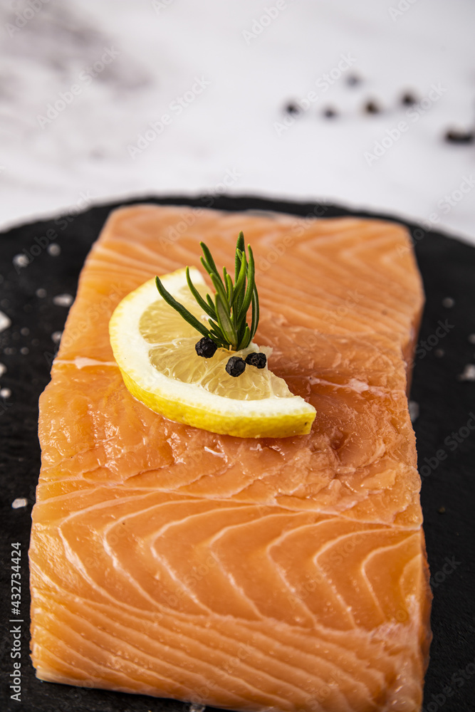 Wall mural Vertical shot of raw salmon fillet on slate plate with lemon and rosemary on the table