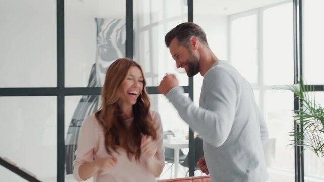 Beautiful young heterosexual couple having fun and dancing at home together