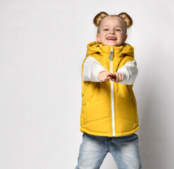 pretty smiling blonde in a yellow puffy vest is standing with her arms outstretched towards you.