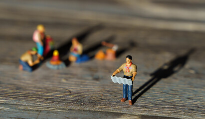 Miniature hikers, model people, camping around a bonfire, on a wooden floor, with their shadows in the background