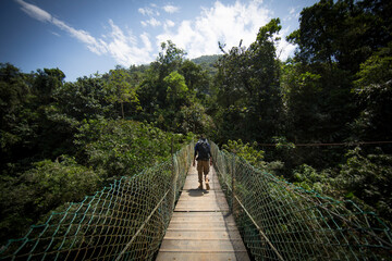 young man crossing a hanging bridge in Sierra Nevada, Colombia - obrazy, fototapety, plakaty