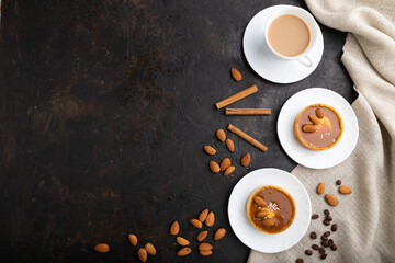Sweet tartlets with almonds and caramel cream with cup of coffee on a black concrete background. flat lay, copy space.