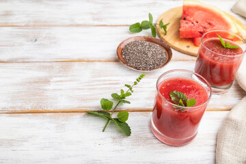 Watermelon juice with chia seeds and mint in glass on a white wooden background with linen textile. Side view,  copy space.