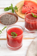 Watermelon juice with chia seeds and mint in glass on a white wooden background with linen textile. Side view.