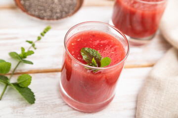 Watermelon juice with chia seeds and mint in glass on a white wooden background with linen textile. Side view, selective focus.