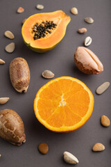 Ripe cut papaya and orange on gray pastel background. Side view, close up.