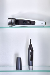 Cosmetic trimmer for nose and ear hair and hairclipper are on shelf of wall cabinet in bathroom.