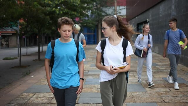 Young students with backpacks and notebooks walk down the street